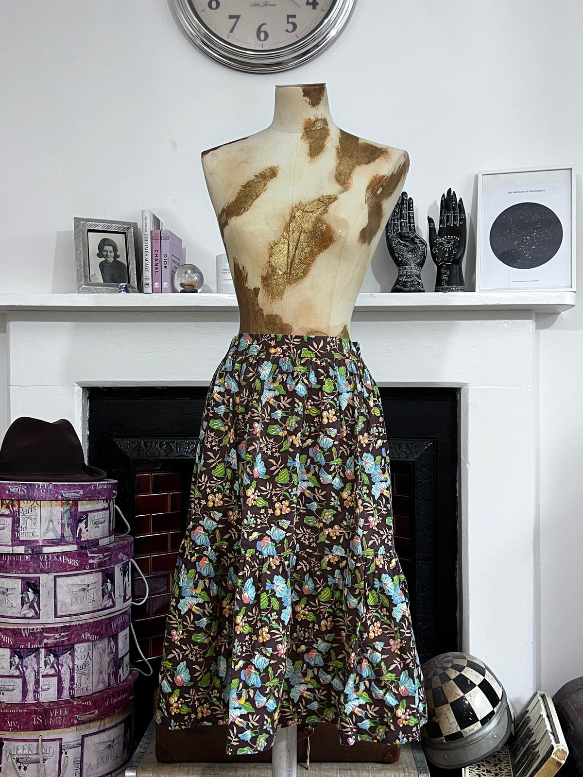 May include: A brown midi skirt with a floral print featuring blue, green, and yellow flowers. The skirt has a gathered waist and a tiered design.